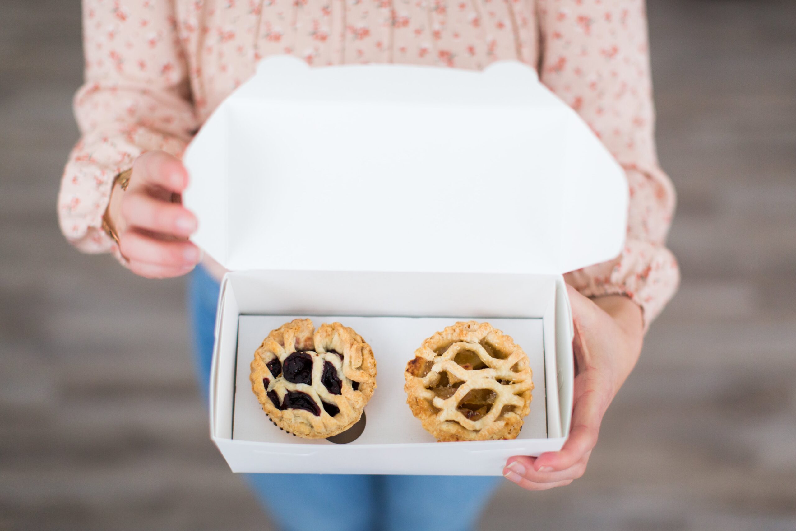 overhead-shot-female-holding-white-box-containing-two-small-pastries-min